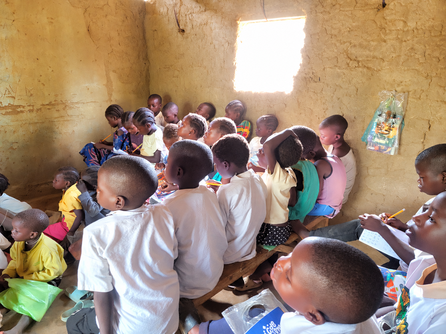 Children sitting together on wooden benches in a classroom.