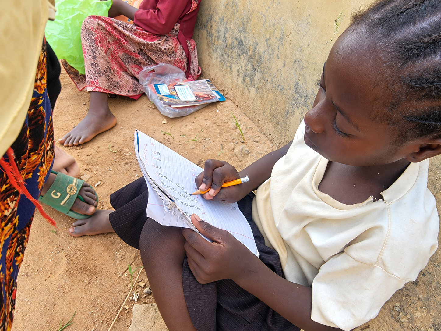 A girl practises letters in her notebook with a pencil.